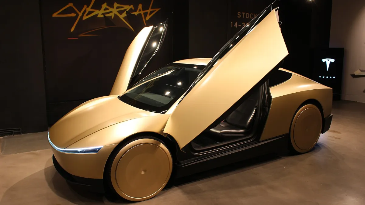A gold Tesla Cybercab with both doors raised. Photograph by Ulf Klingström, public domain.
