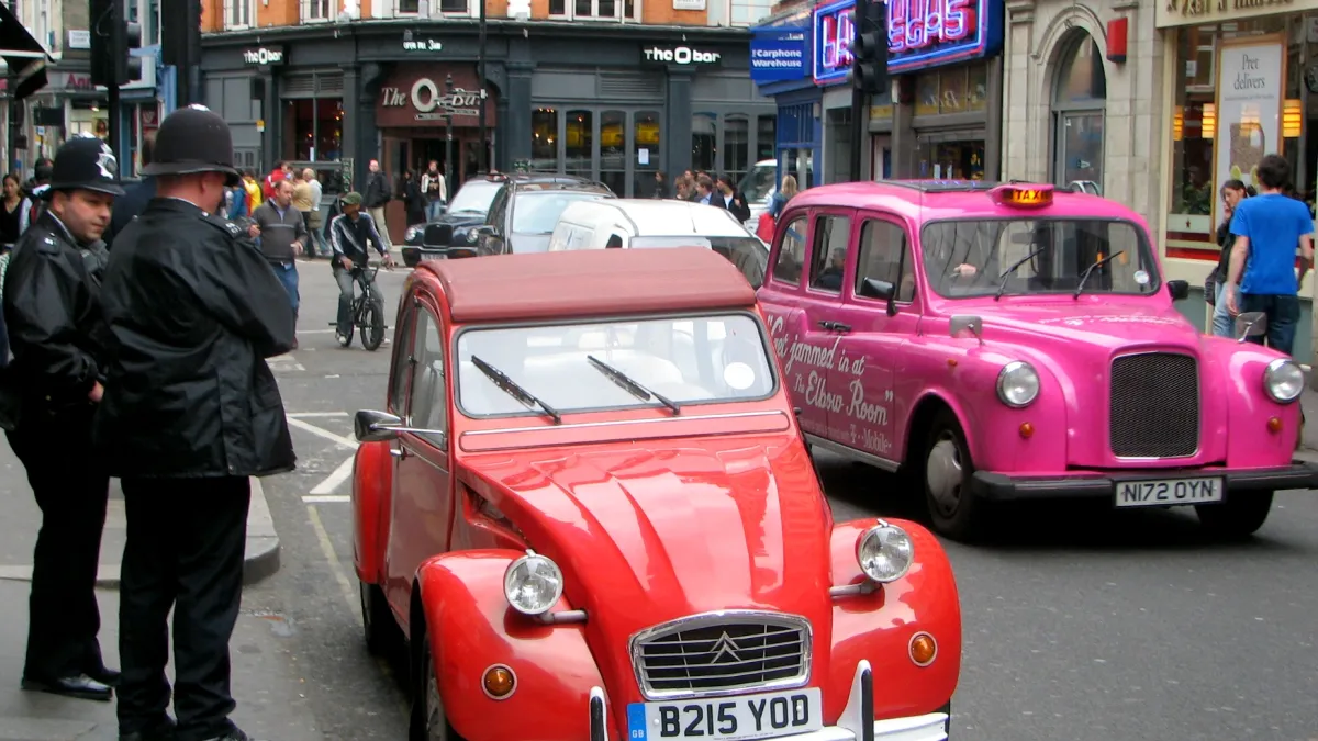 Two British police officers on Wardour Street in Soho, with a pink London taxi beside them