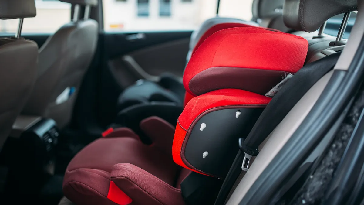 High-back child booster seat fitted on a car’s rear seat with the adult seat belt routed through it.